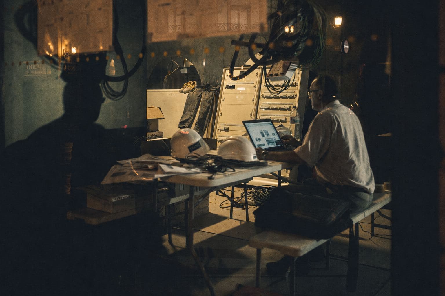An engineer working from a laptop on a folding table on a factory floor, hard hats beside him.